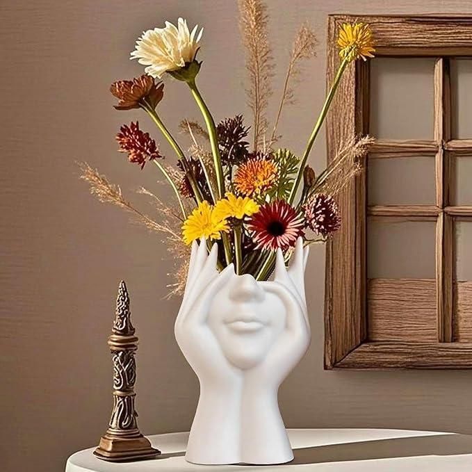 White vase shaped like a face with flowers on a neutral background