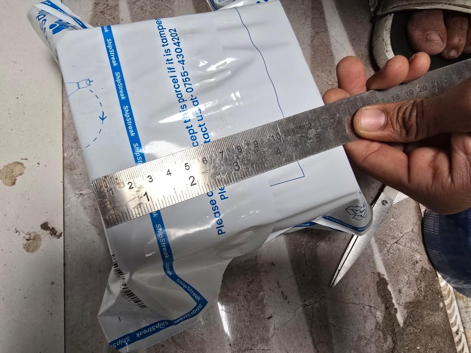 Hand holding a ruler over a medical package on a concrete floor.