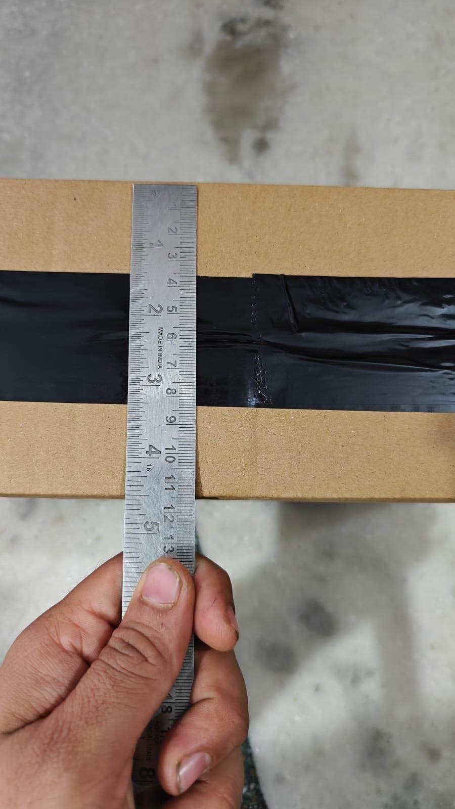 Hand holding a ruler against a cardboard box on a textured surface