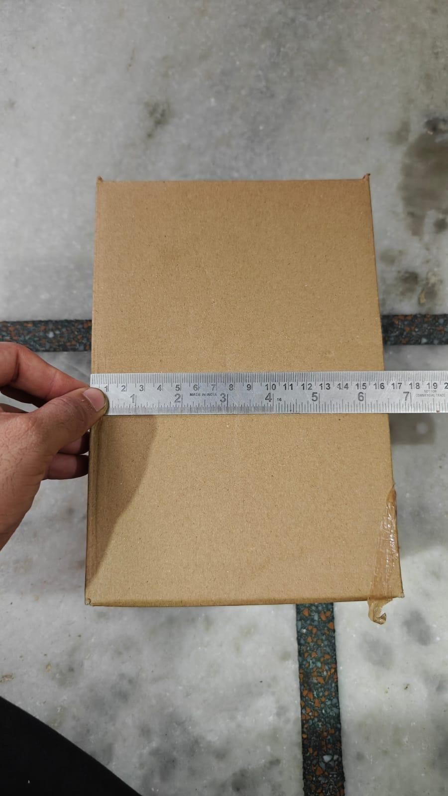 Kraft paper box being measured with a ruler on a concrete floor.