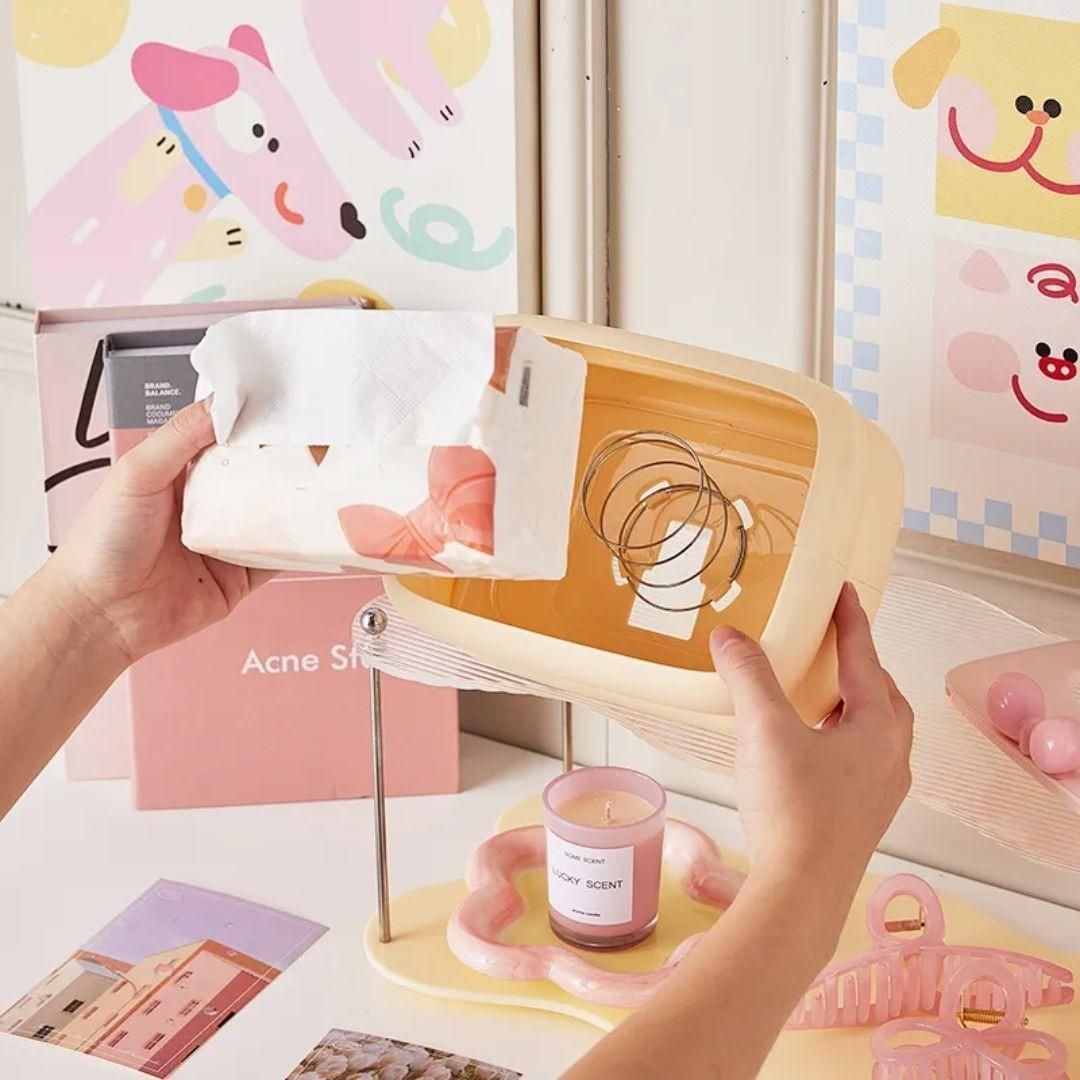 Person holding a small wooden tray with a pink candle and decorative items against a colorful background.