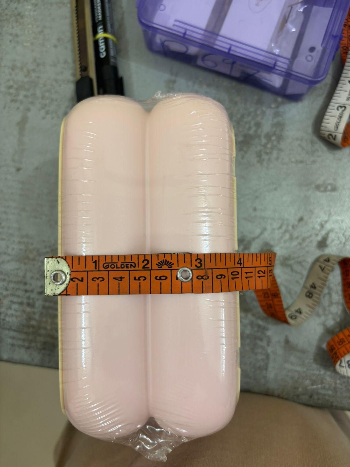 Two cylindrical objects wrapped in plastic with a measuring tape on top, on a concrete surface.