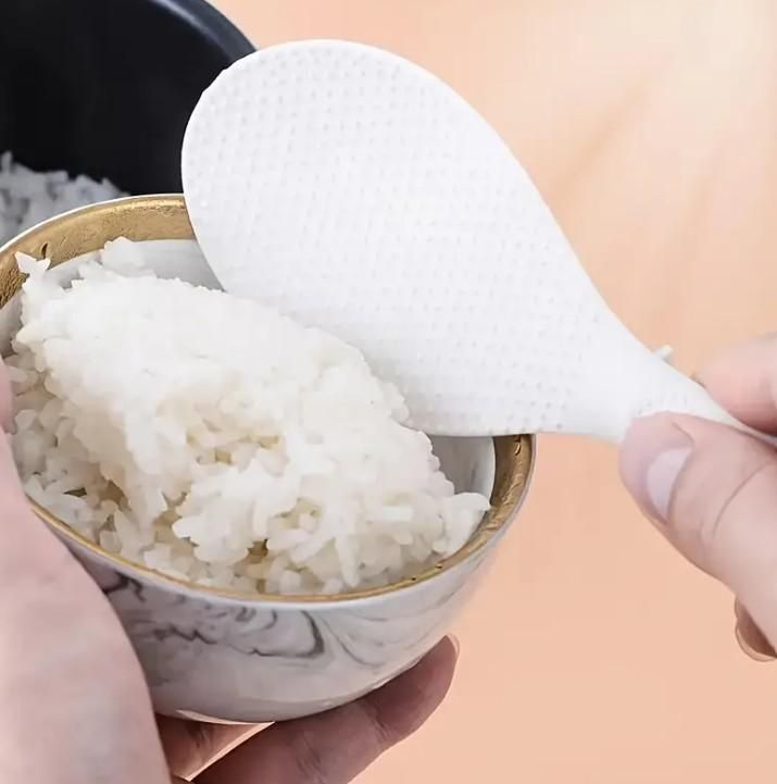 White rice paddle being used to scoop white rice from a bowl.