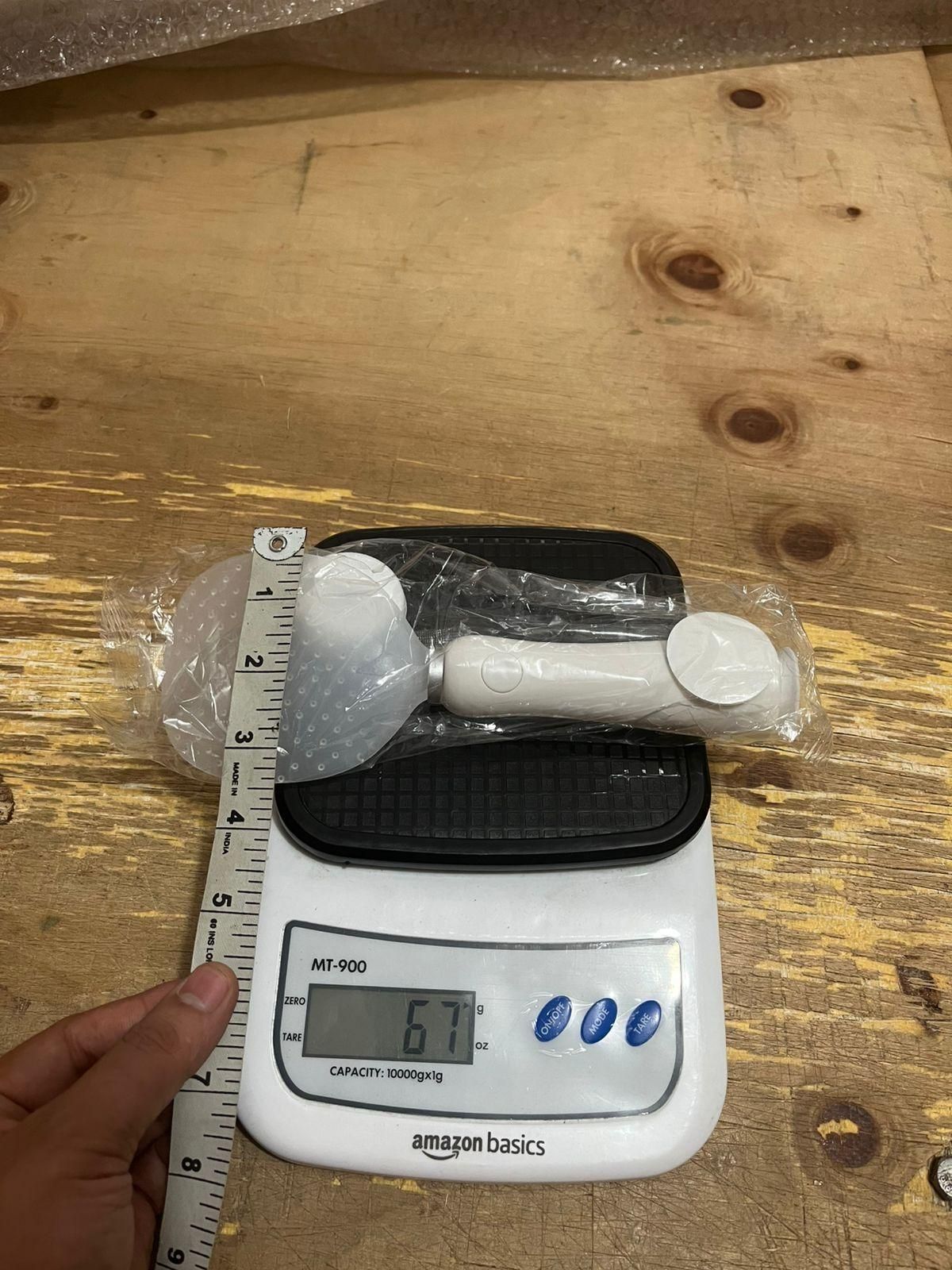 White handheld tool on a digital scale with a ruler for measurement on a wooden surface