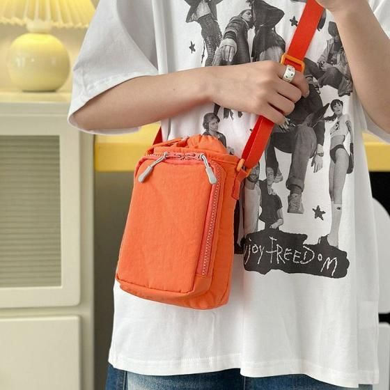 Person holding an orange crossbody bag with a graphic t-shirt in the background