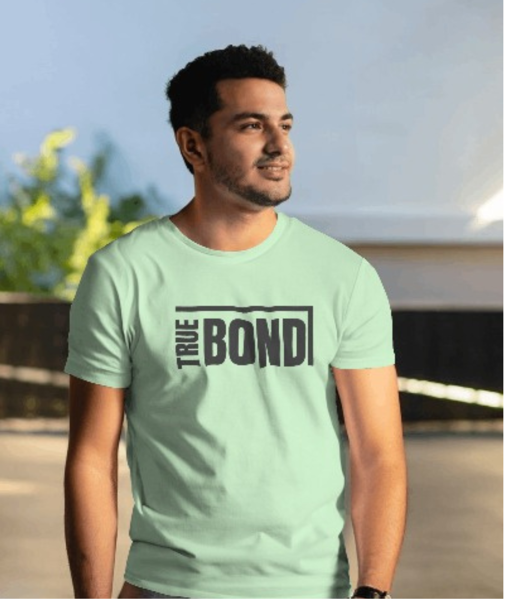 Man wearing a light green t-shirt with 'True Bond' text outdoors.